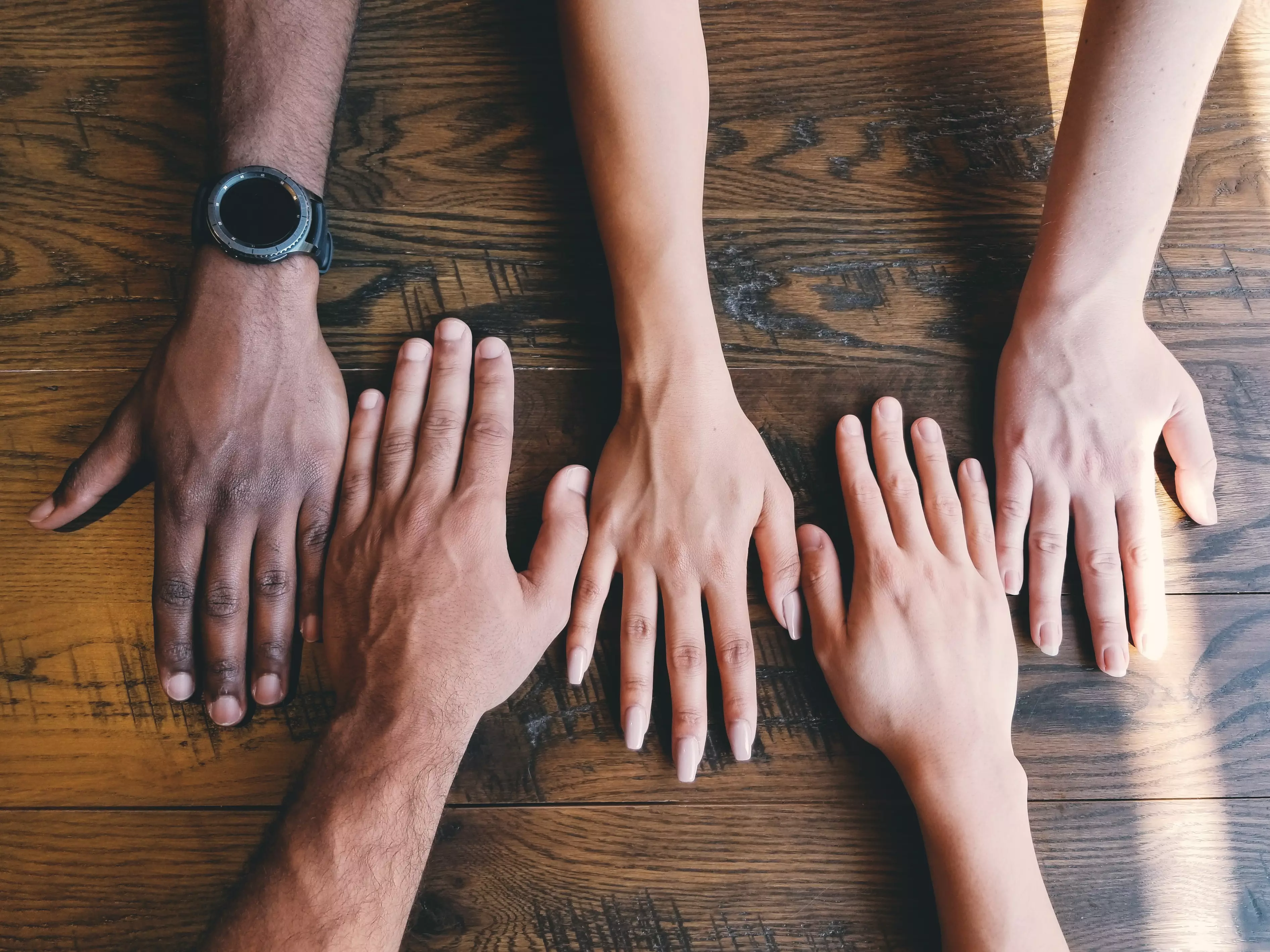 Empleados de diferentes razas, con las manos juntas, uno al lado del otro.